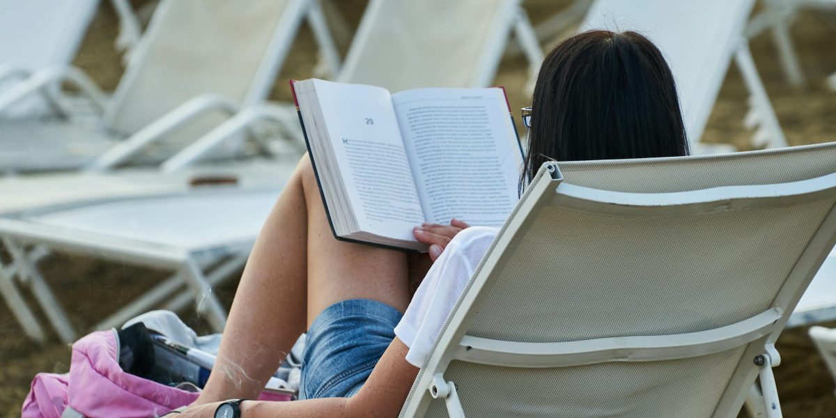 A person relaxes by the ocean, enjoying a lighthearted book, embodying the coastal escape provided by humorous series.